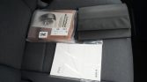 Car seat with two document bundles: a black leather folder and a sealed orange warranty manual labeled SNE, plus a white PVS booklet in plastic.