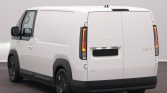 Rear three-quarter view of a white cargo van with closed rear doors and vertical taillights, parked indoors on a gray floor.