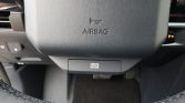 Steering wheel with 'AIRBAG' label and a hidden drive mode switch below the airbag area in a car cockpit.