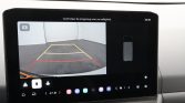 Rearview camera feed showing a parking space with yellow guide box and a red safety zone on the ground, displayed on the car dashboard screen.