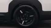 Close-up of a black Kia wheel with aero-style spokes and white reflective strips, mounted on a white vehicle.