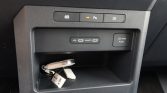 Center console in a car showing a USB-C/USB-A charging area, 12V outlet, and a small open storage pocket with keys inside