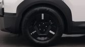 Close-up of a white SUV’s front left wheel, showing a black angular hubcap with white rectangular decals and lug bolts visible at the center.