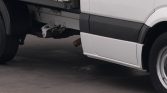 Side view of a white truck showing the undercarriage, hitch assembly, and exposed exhaust pipe beneath the cargo area.