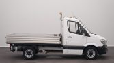 Side profile of a white flatbed utility truck with an open cargo bed, indoors in a neutral setting.