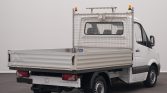 White Mercedes-Benz Sprinter utility van with an open flatbed and metal mesh cargo barrier at the rear, incl. amber warning lights on top.