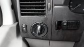 Dashboard of a vehicle: left air vent, dimmer switch, and a circular headlight control dial with off and light icons; to the right, a black switch panel with an white 'H'-shaped symbol.