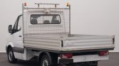 Rear view of a white flatbed truck with a metal mesh cabin guard, parked indoors.