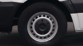 Close-up of a vehicle wheel: steel rim with circular holes and a black tire on a white van.