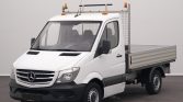 White Mercedes utility truck with a flatbed and metal cage behind the cab, parked indoors.