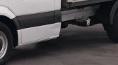 White truck side with damaged lower panel and exposed hitch undercarriage, parked on pavement
