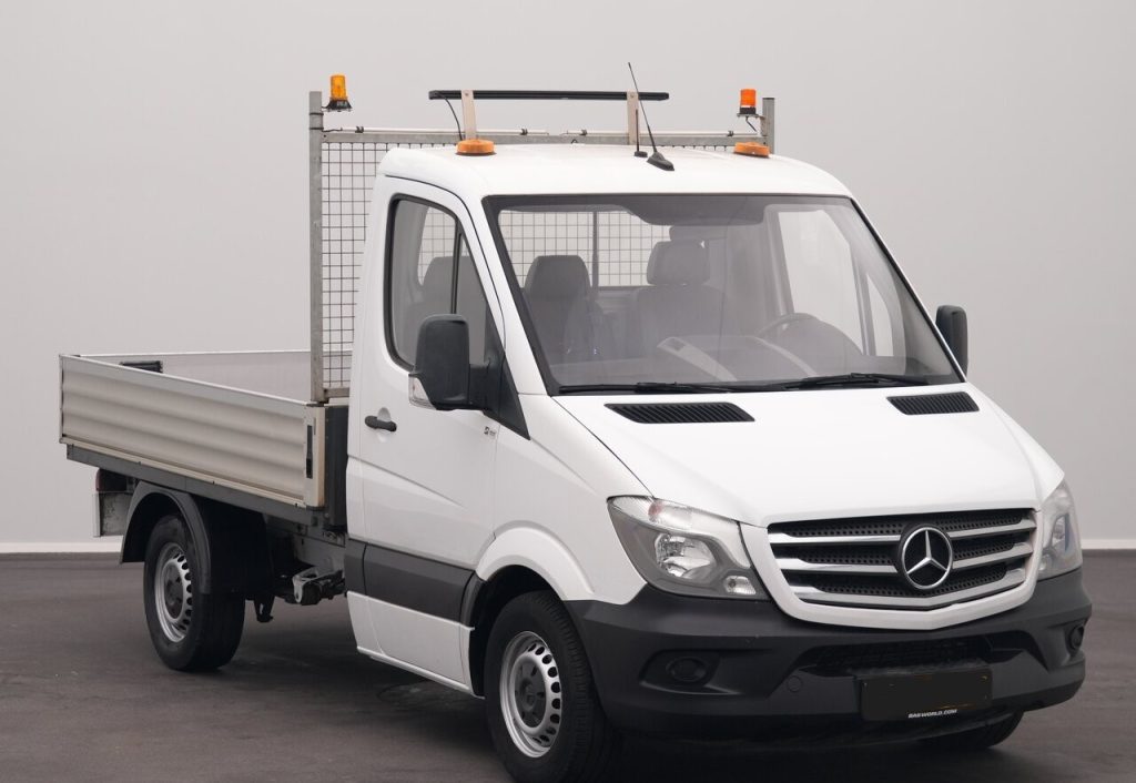 White Mercedes-Benz flatbed work truck with an open cargo bed and mesh rear cage, topped with orange beacon lights on the cab roof