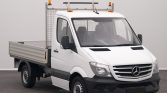 White Mercedes-Benz flatbed work truck with an open cargo bed and mesh rear cage, topped with orange beacon lights on the cab roof