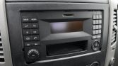 Car stereo head unit in a vehicle with labeled buttons (Radio, Media, Tel, Sys) and a numeric keypad on the right, small screen in the center, and knobs below.