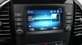 Car infotainment touchscreen showing FM-radio with 'Popmuziek' and playback controls; Dutch UI and side buttons visible.