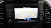Car infotainment screen showing a rearview camera with yellow guide lines and a red line; Dutch warning text above: 'Omgeving in acht nemen!'