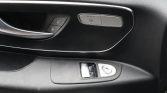 Car interior door panel with silver-accented door handle, seat heater button, and window/mirror controls on a black dashboard surface.