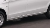 White van side view with a two-panel door, visible 'Electric' badge near the front and a wheel at the left, resting on pavement.