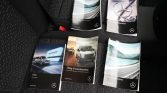 Mercedes-Benz vehicle manuals and instruction books spread on a car seat in a dark fabric interior.