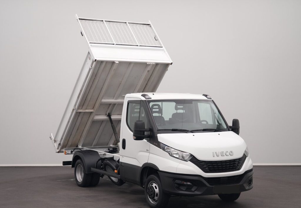 White Iveco dump truck with the cargo bed lifted, ready to unload in a neutral indoor setting.