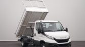 White Iveco dump truck with the cargo bed lifted, ready to unload in a neutral indoor setting.