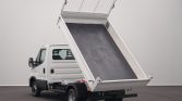White dump truck with its cargo bed raised for unloading, viewed from the rear-left side in a neutral setting.