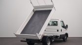 White dump truck with its hydraulic bed raised, ready to unload material in a plain indoor setting