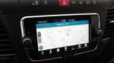 Touchscreen car navigation showing a map with a blue top bar and route indicator on the center console