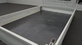 White flatbed truck with grey bed surface and metal side rails, featuring a mesh cab divider at the front edge of the bed.