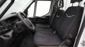 Interior of a white cargo van showing the driver’s seat, steering wheel, and three front seats with dark upholstery and dashboard details visible