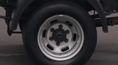 Close-up of a heavy-duty truck wheel: silver steel rim with six lug nuts and a black tire, viewed from the side under the fender.