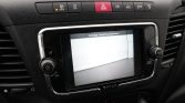 Car dashboard with a touchscreen displaying a rear-view camera feed of a parking area; the hazard button and other controls are visible above the screen.