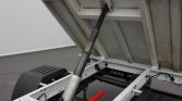 Hydraulic lift cylinder raises a dump bed on a trailer, viewed from below.