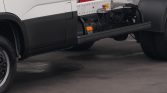 Side view of a white commercial truck with its chassis and mounting rails exposed, wheel on the left and an orange marker light visible under the frame