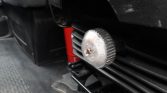 Close-up of a knurled metal adjustment dial on a black engine component, with a red spring behind and a scale from 0 to 50 visible.