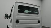 Rear view of a white cargo van with a windowed back door, two black vents, and a visible side mirror in a plain studio.
