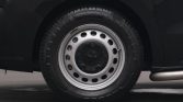 Close-up of a car's silver steel wheel with circular holes and black tire, mounted on a dark vehicle.
