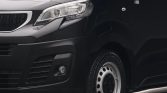 Close-up of the front left side of a black van, showing headlight, grille, and front wheel with a steel rim.
