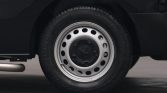 Close-up of a car wheel with a silver steel rim and black center cap featuring a lug pattern and circular holes in the rim edge.