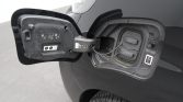 Open fuel-filler door on a black car, exposing the fuel cap and tethered cap near the rear wheel.