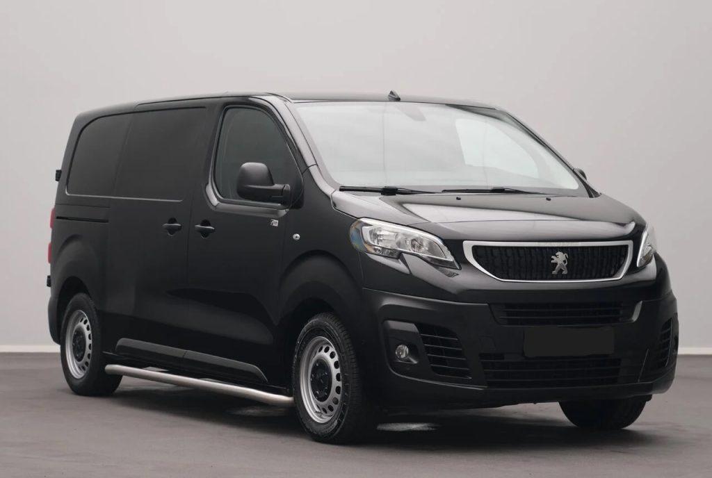 Front three-quarter view of a black Peugeot cargo van parked indoors, showing its grille with the lion badge and silver side step on the near side.
