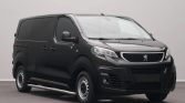 Front three-quarter view of a black Peugeot cargo van parked indoors, showing its grille with the lion badge and silver side step on the near side.