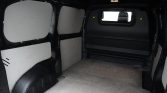Interior of an empty cargo van with gray wall panels and a small rear window at the far end.