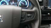 Close-up of a car steering wheel with mounted media controls and blue-illuminated dashboard gauges in the background.