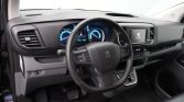 Interior view of a Peugeot car: steering wheel, digital instrument cluster, and center touchscreen visible on the dashboard (peugeot logo on screen).