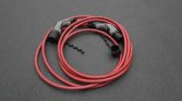 Coiled red electric vehicle charging cable with connectors on a dark surface.