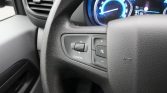 Close-up of a car steering wheel with left-side control panel including a CONFIG knob and plus/minus and mute buttons.